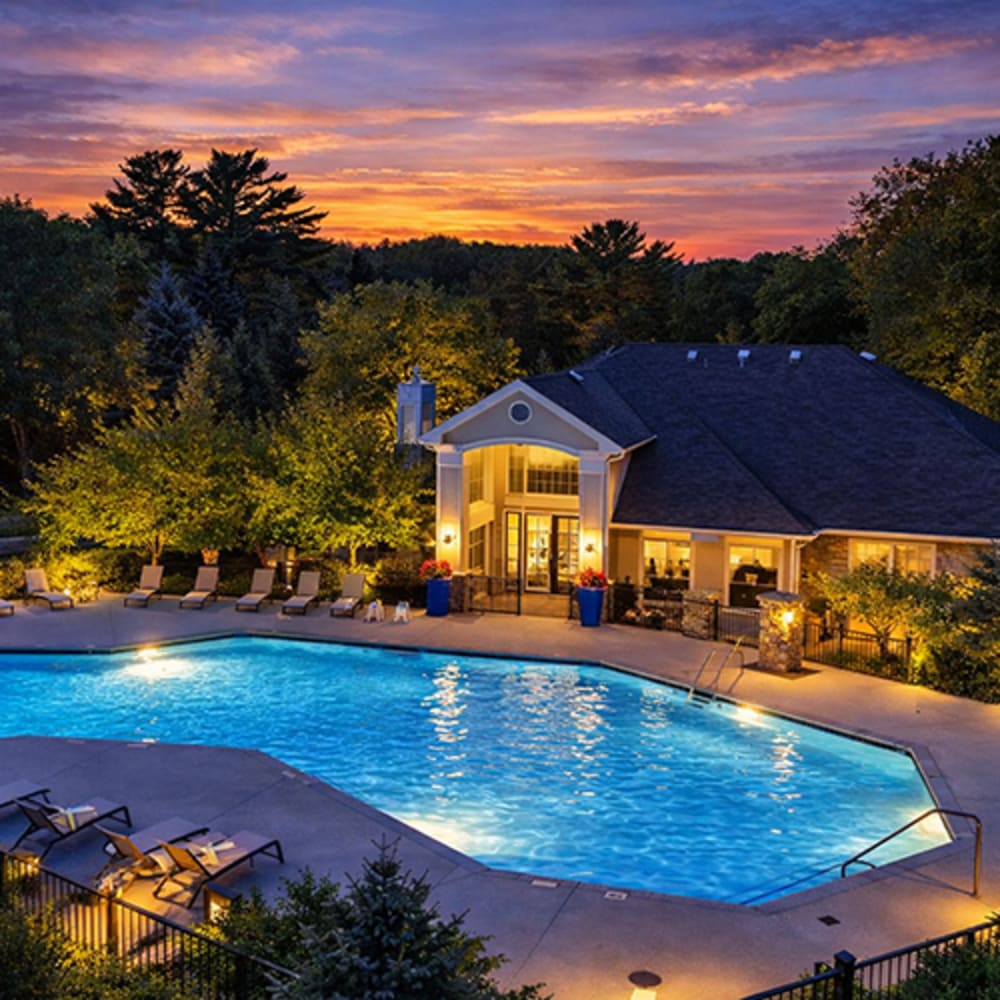 Sparkling resort-style pool with lounge chairs and a clubhouse surrounded by greenery at sunset at 43 North Apartments in Grand Haven, Michigan