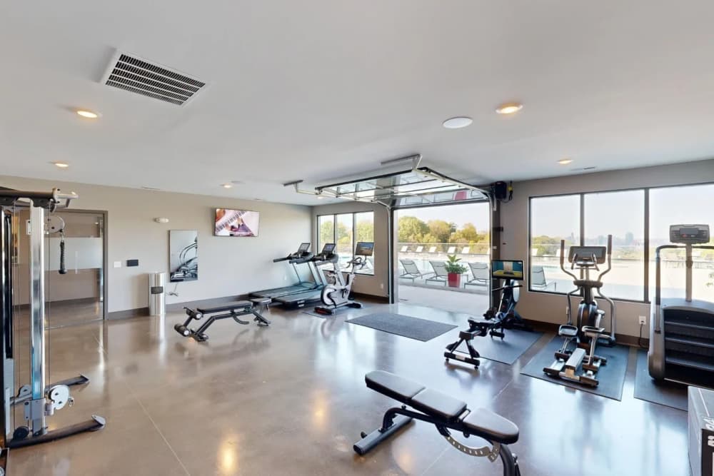 Fitness center at Elevation 800 featuring treadmills, bikes, strength equipment, and large windows with views of the pool deck and surrounding greenery.