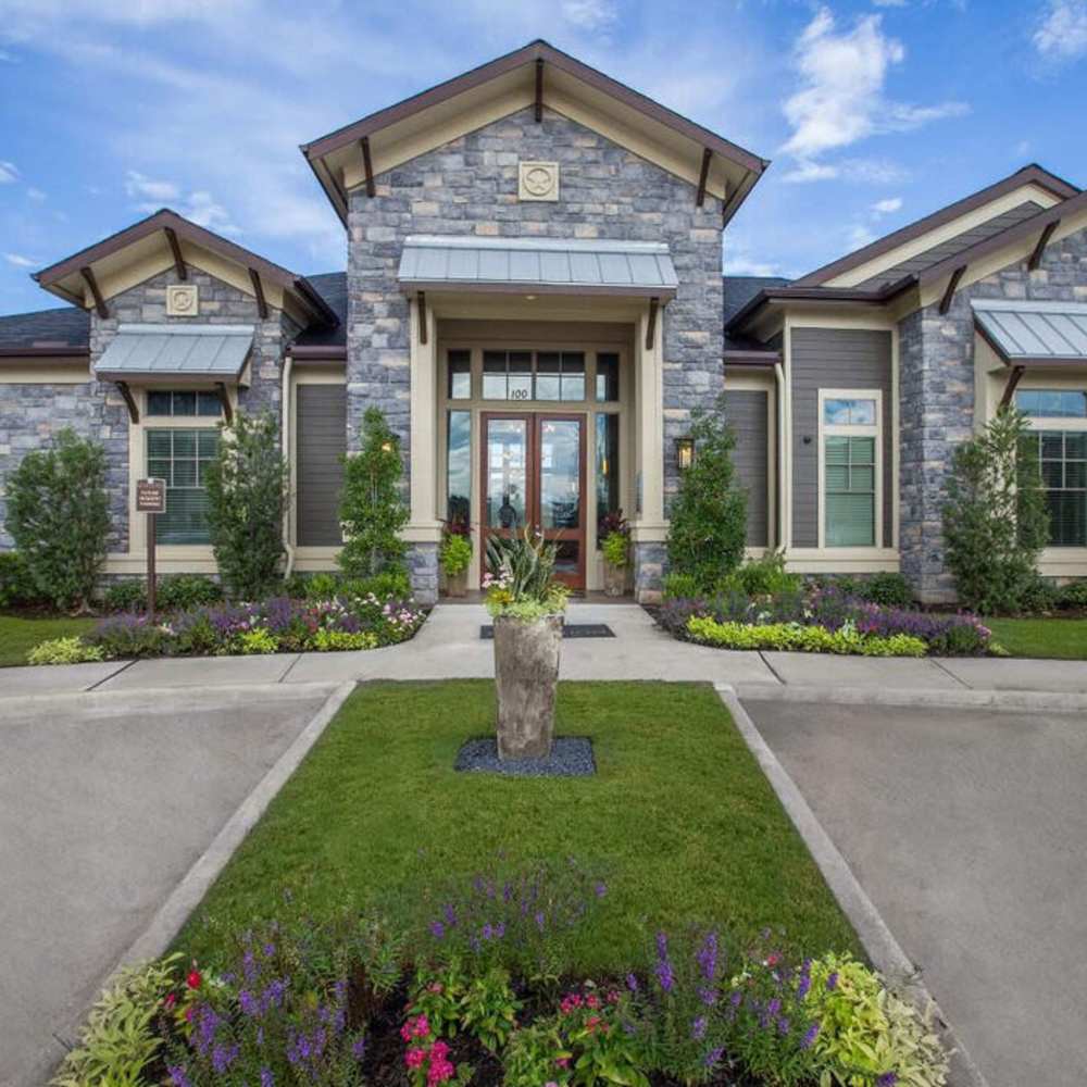 Elegant stone entrance with landscaped gardens and vibrant flowers, welcoming atmosphere and gated access at Plantation Park Apartments in Lake Jackson, Texas
