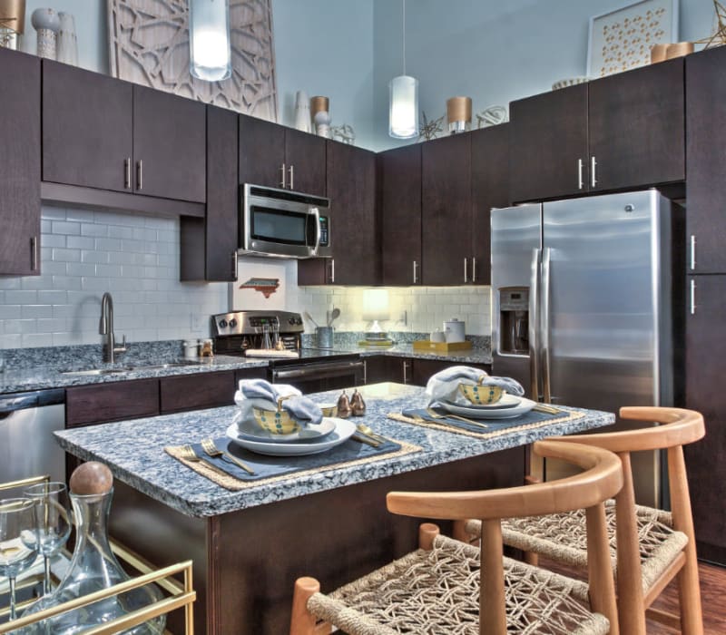 Chic styled kitchen with stainless steel appliances, granite counters, and dark wood cabinets at Marq Midtown 205 in Charlotte, North Carolina