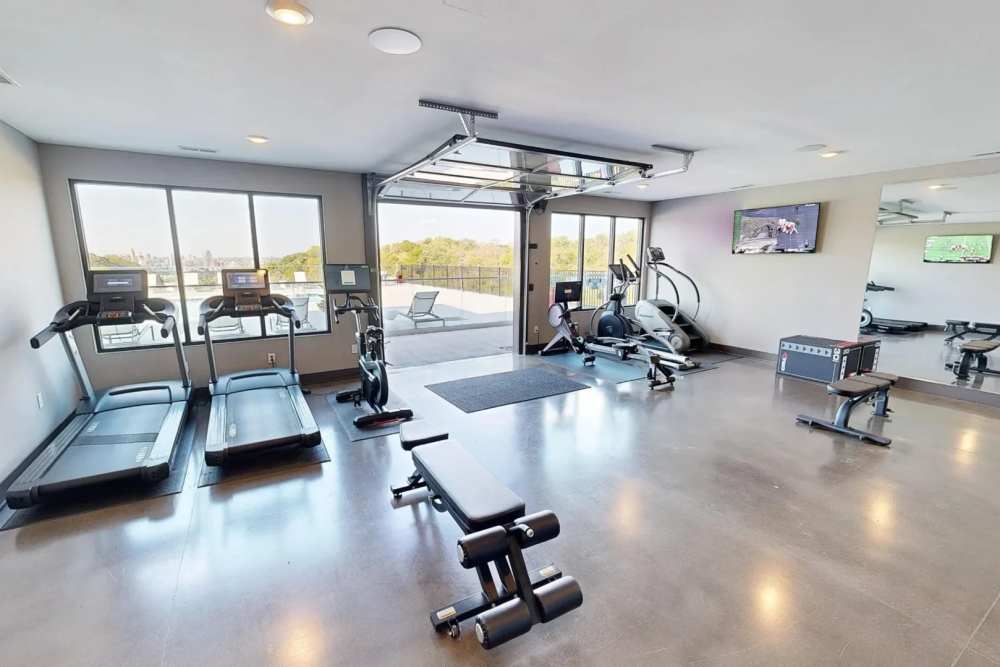 Modern fitness center at Elevation 800 featuring treadmills, ellipticals, strength equipment, and a garage-style door opening to the outdoor pool deck.
