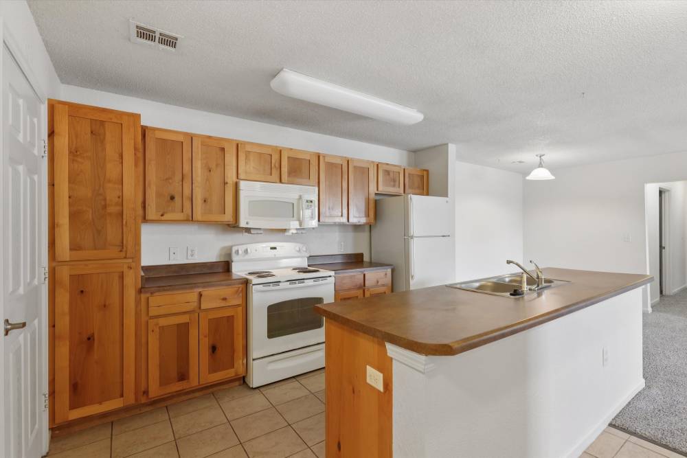Charming modern kitchen with warm wooden cabinetry and inviting tile floors at Covington Woods Apartments in Lansing, Kansas.