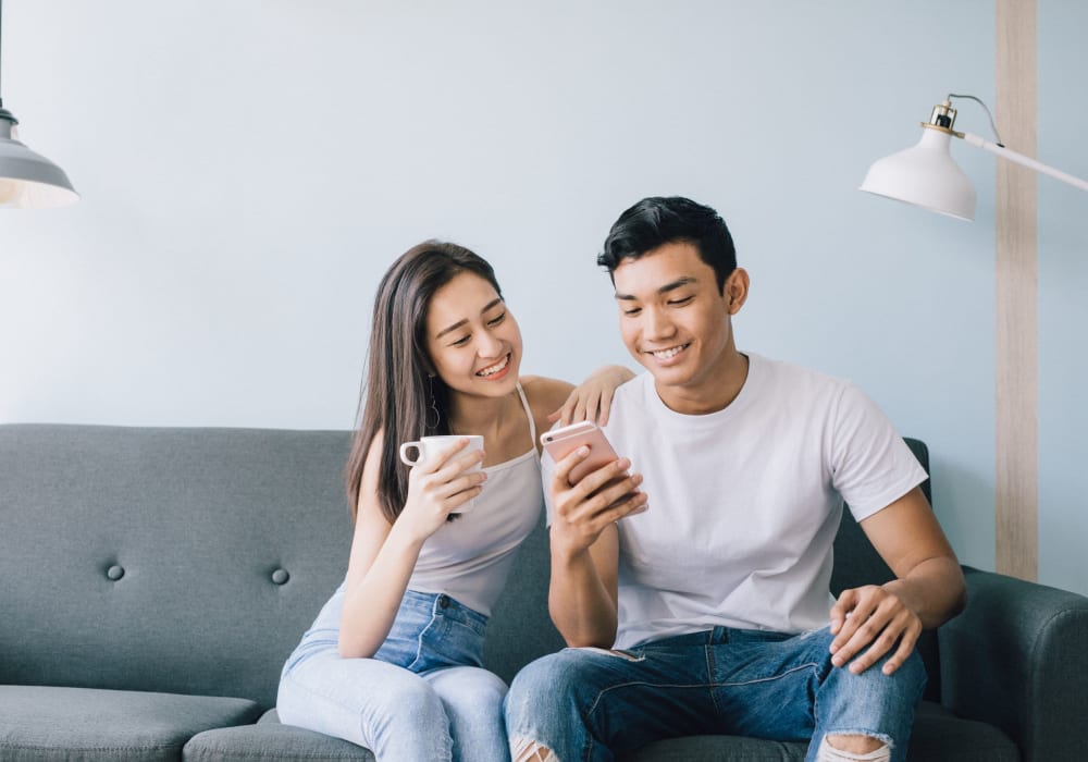 Couple enjoying the comfy couch while browsing the web on their phones at Park Lane Apartments in Little Falls, New Jersey