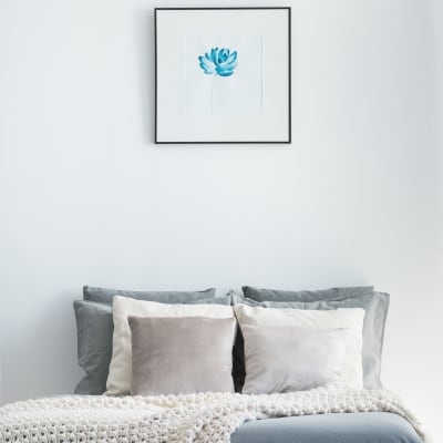 Decorative pillows on the bed with a simple painting of a blue flower hung above in a model home's bedroom at Sofi Belmont Glen in Belmont, California