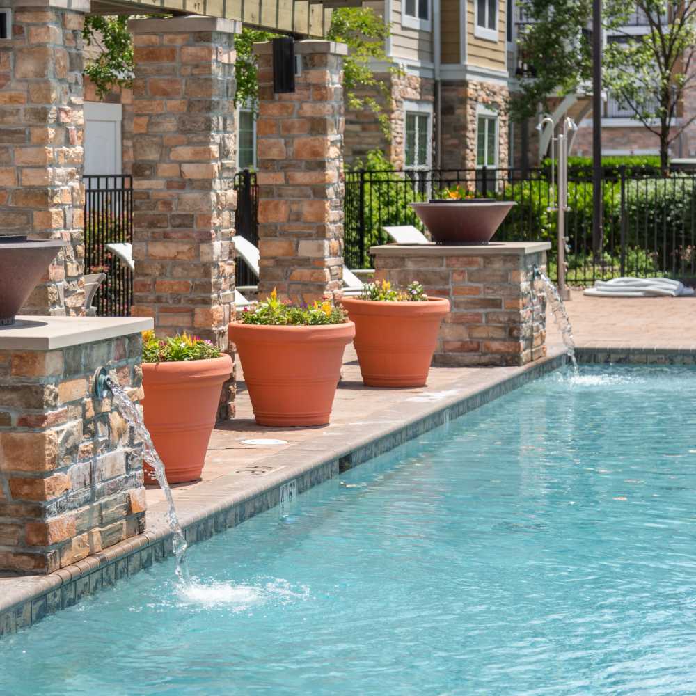 Outdoor poolside scene with cascading water features on stone pillars at Red Knot at Edinburgh in Chesapeake, Virginia.
