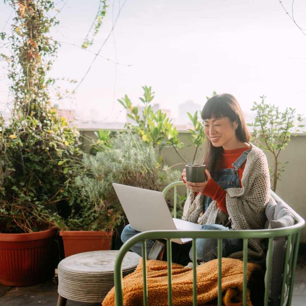 Cozy balcony with lush plants and a woman sipping coffee at Antioch Family & Senior Apartments in Antioch, California
