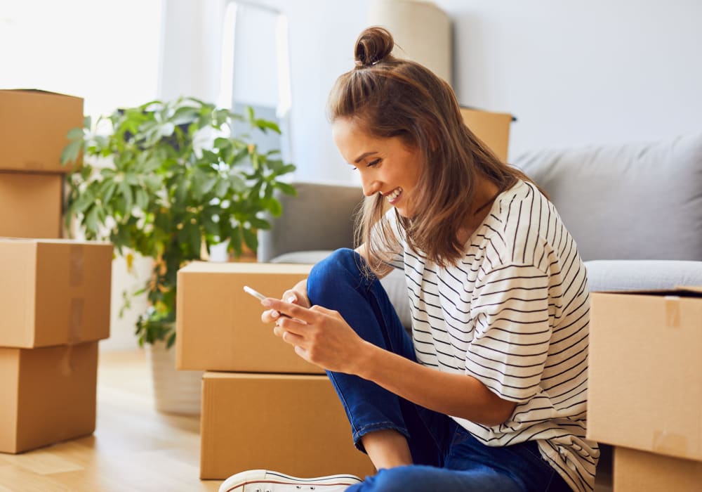 Woman sitting on floor typing on her phone while surrounded by moving boxes at YourSpace Storage