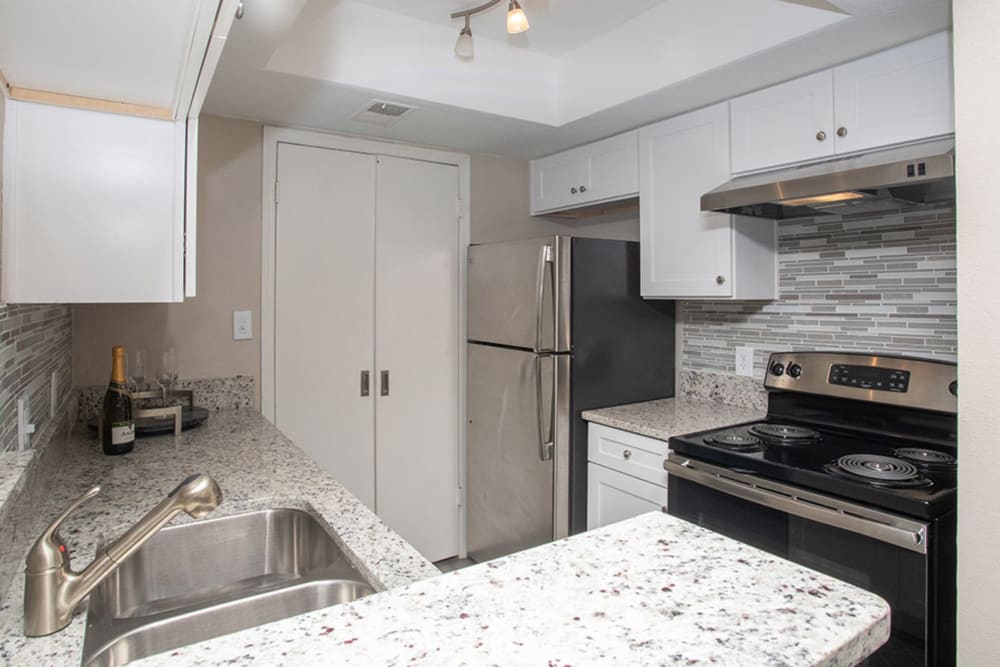 Modern kitchen with stainless steel appliances, granite countertops, and a tile backsplash at Castlegate Collier Hills in Atlanta, Georgia