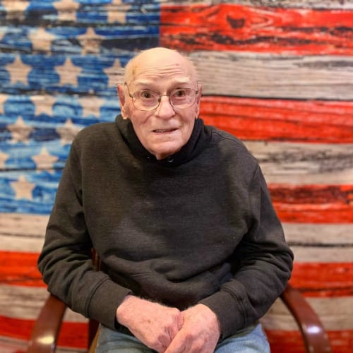 Resident sitting and smiling in front of an american flag at Oxford Glen Memory Care at Owasso in Owasso, Oklahoma