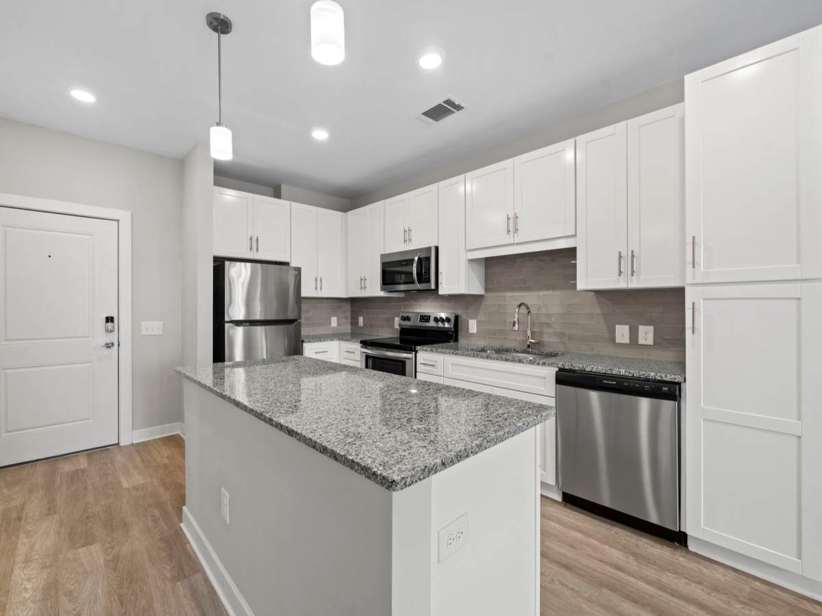Open kitchen with stainless-steel appliances, white wood cabinet, island countertop and barstool at The Rise at Regency in Henrico, Virginia