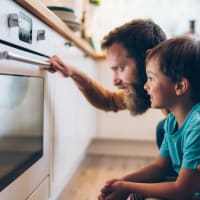 Resident dad and his son looking eagerly in oven and waiting for what they're making to finish cooking at Decker Apartment Homes in Ft Worth, Texas