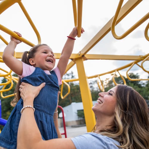 A mother holding her child up on the monkeybars at Verandahs at Cliffside Apartments in Arlington, Texas