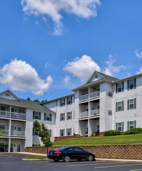 White apartment buildings with balconies and greenery at Beaumont Greene Senior Living in Athens, Ohio