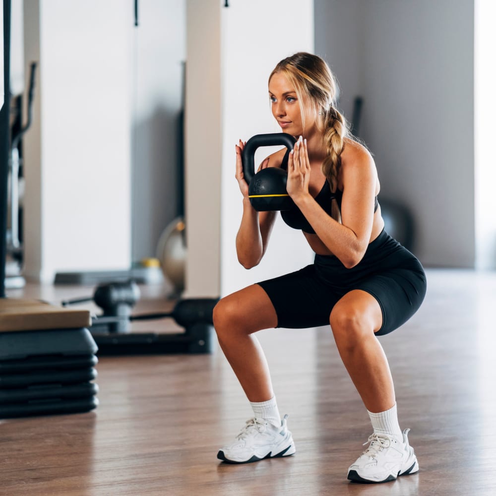 Resident doing some squats while holding a kettlebell in the fitness center at Anden in Weymouth, Massachusetts