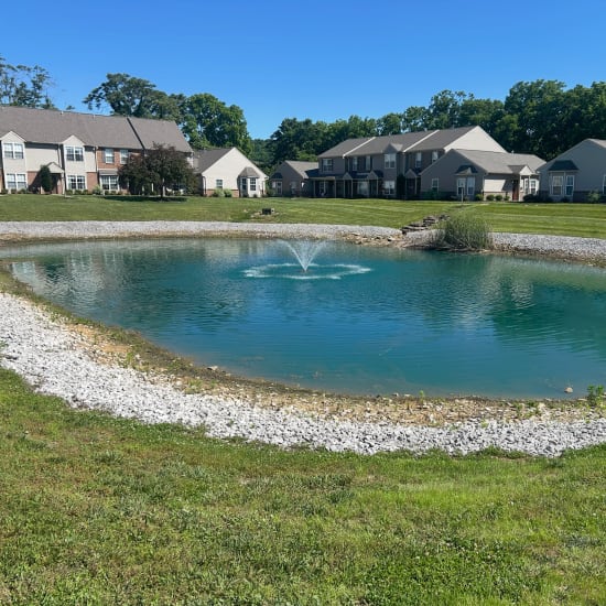Pond with fountain and landscaped grounds at Whispering Wind Apartments & Townhomes in Newtown, Ohio