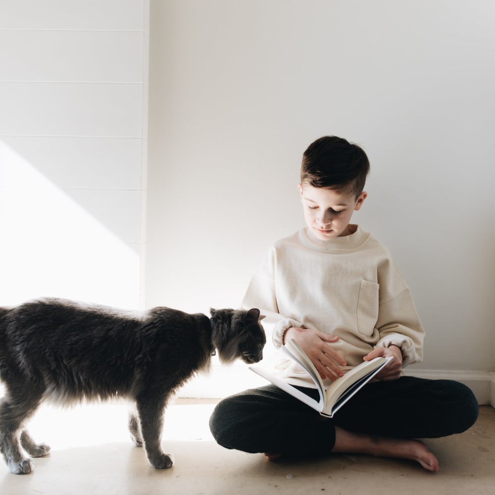 Kid sitting on the floor with a book and his cat at The Columns at Westchase in Houston, Texas