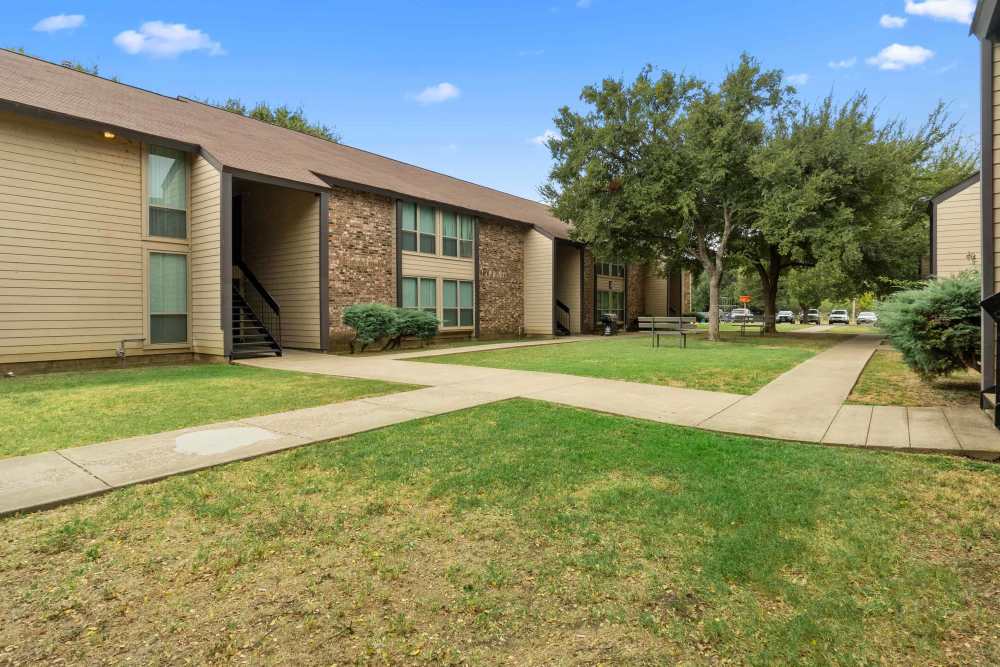 Exterior view of the apartment surrounded by trees and walkways with lush green area at Woodland Village Apartments in Breckenridge, Texas