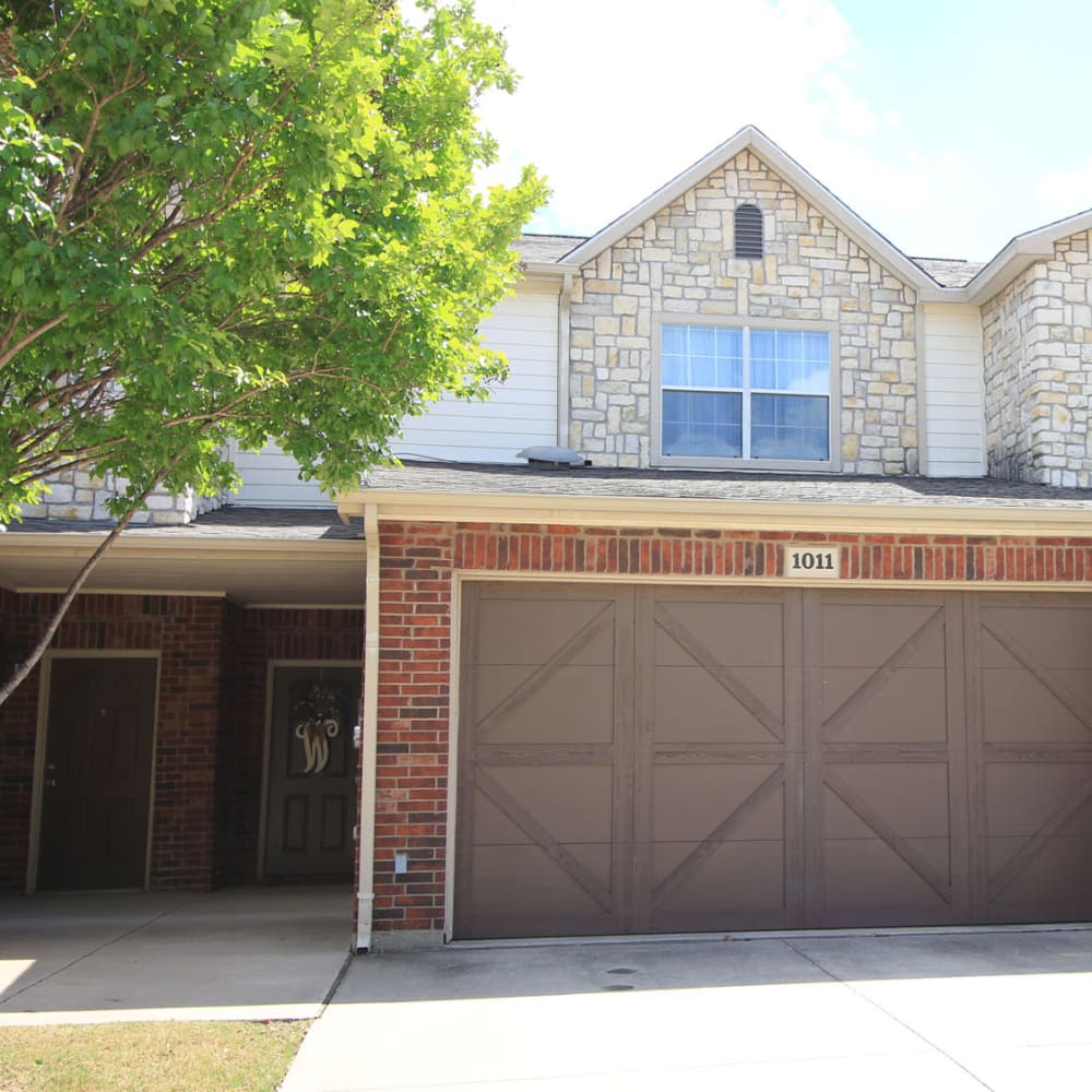 Mature tree and a private garage outside the entrance to a townhome at Oaks Estates of Coppell in Coppell, Texas