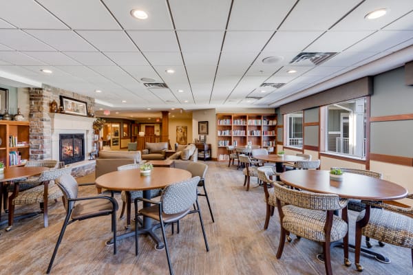 Bistro lounge with round tables, couches, fireplace and books at Arbor Glen Senior Living in Lake Elmo, Minnesota