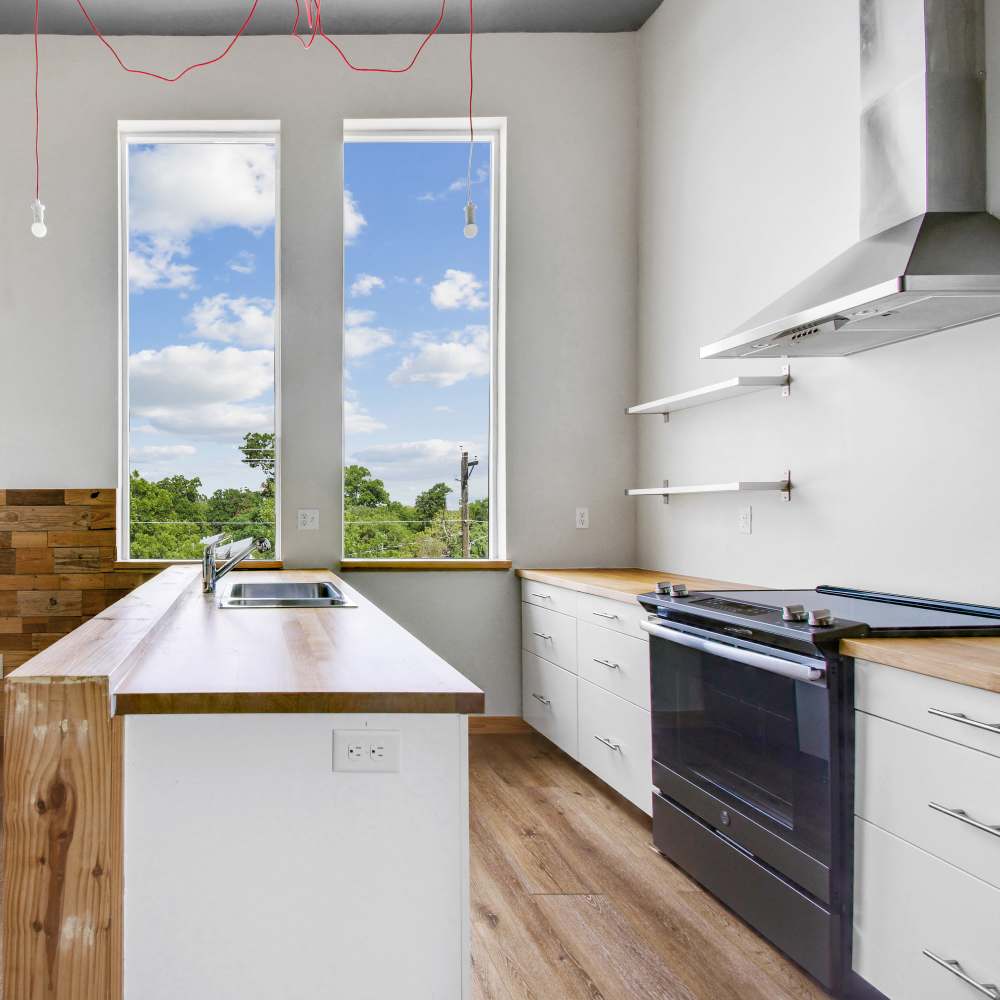 Modern kitchen with stove, sink, stainless-steel hood and large window at The Lofts at 305 in Bryan, Texas