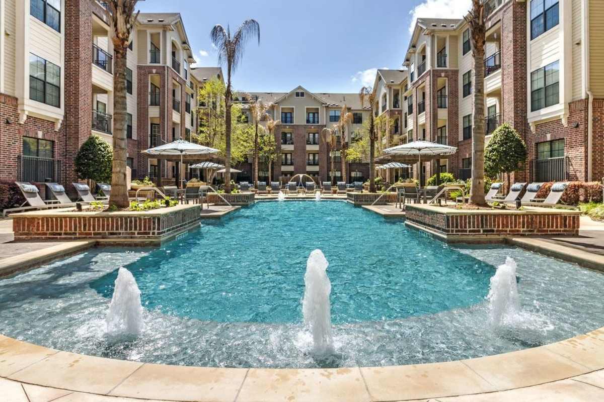 Landscaped swimming pool area surrounded by palm trees and lounge chairs at an apartment complex at Villas At Bunker Hill, Houston, Texas