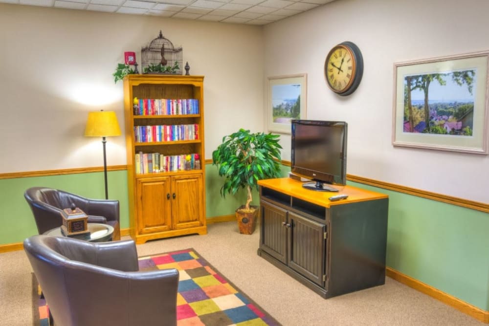 Common area with a bookshelf and two leather chairs at Addington Place of Fort Madison in Fort Madison, Iowa