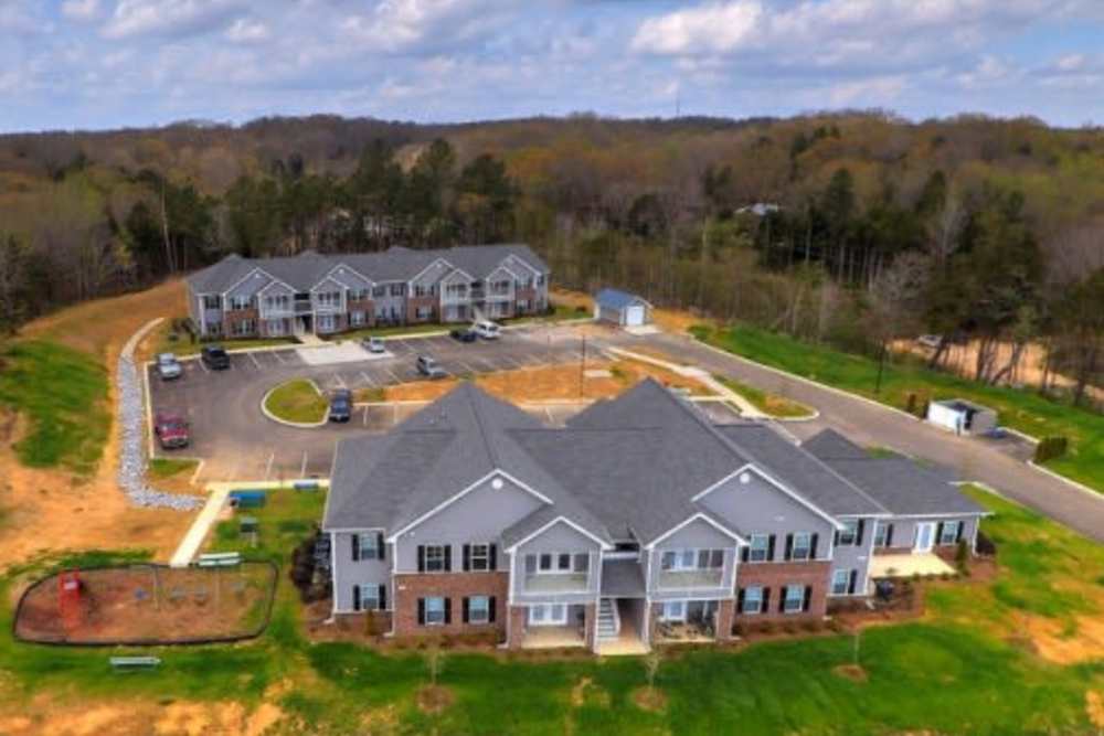 Aerial view of apartment community with parking, playground, and green space surrounded by trees at Oliver Crossing in Linden, Tennessee