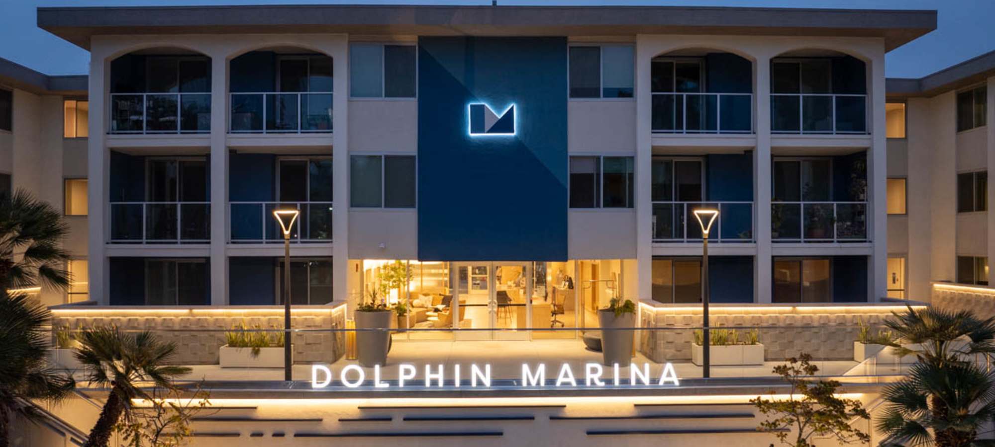 Modern apartment community entrance with illuminated sign and lush landscaping at Dolphin Marina Apartments in Marina Del Rey, California