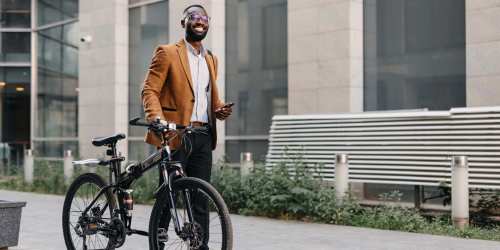 Man in stylish suit smiling beside bicycle in urban setting at Trolley Court in San Diego, California