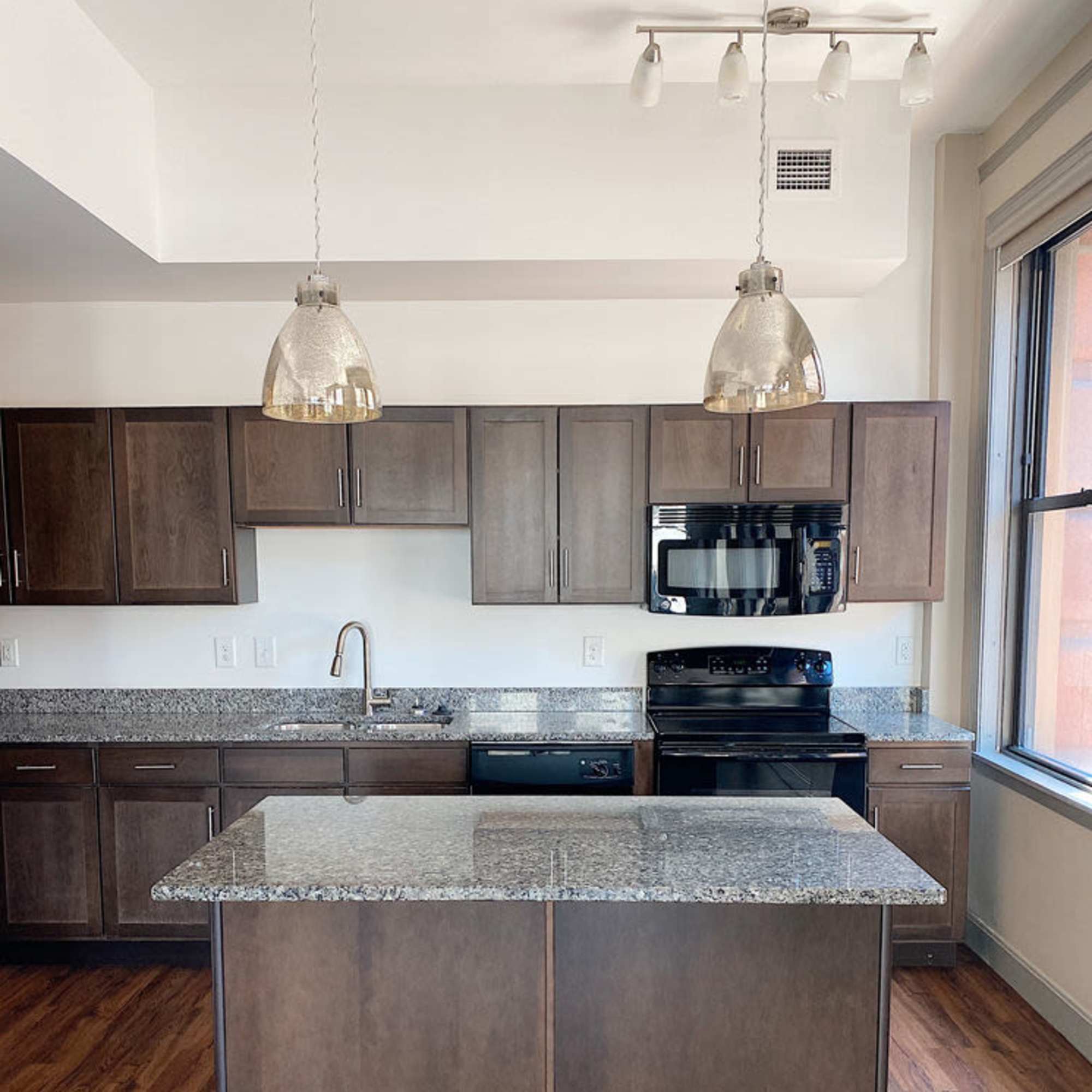 Kitchen with black appliances and wood-style flooring at The Atlas in Columbus, Ohio