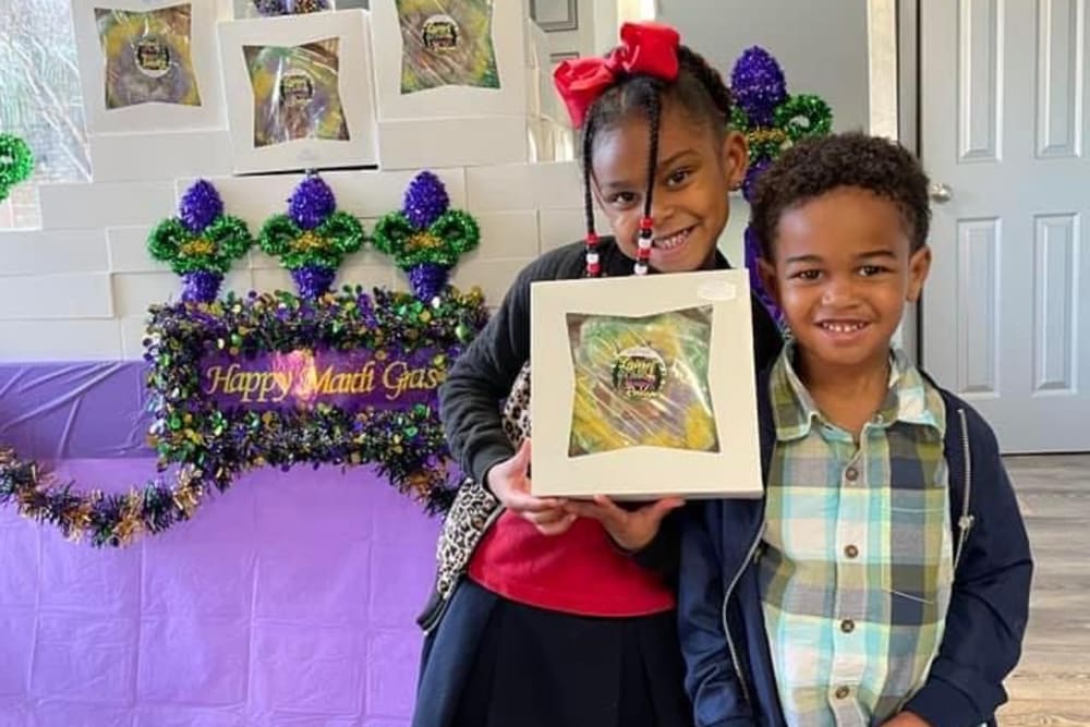 Two kids holding up a Mardi Gras sign at The Mayfair Apartment Homes in New Orleans, Louisiana