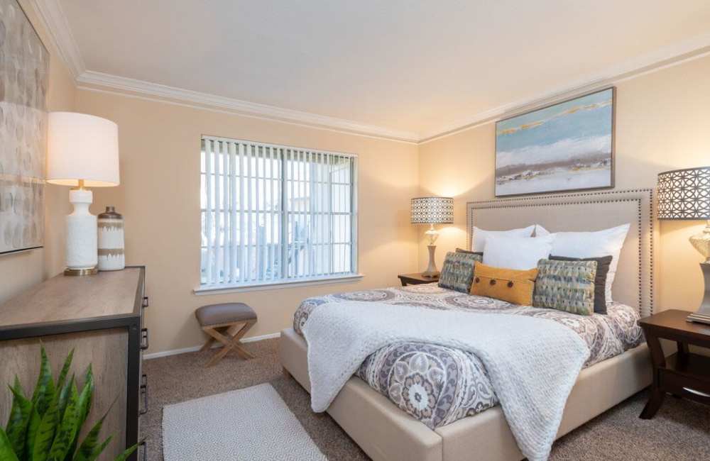 Comfortable bedroom with king size bed, side table lamp and large window at The Pines of Palos Verdes in Mesquite, Texas