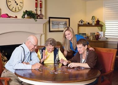 Residents working on a puzzle while caregiver looks on at Burr Ridge Senior Living in Burr Ridge, IL