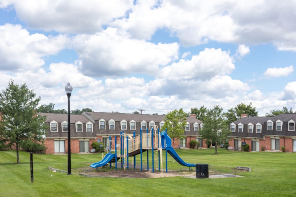 Playground with blue slides and greenery surrounded by brick apartment buildings and bright skies at Dutch Village Apartments in Baltimore, Maryland