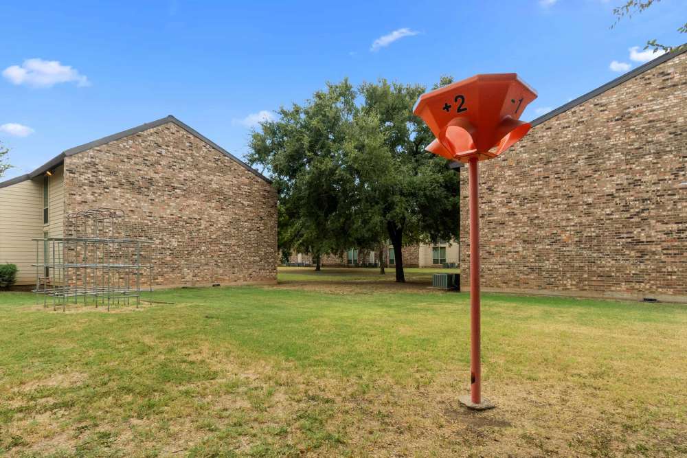 Child play area with a red funnel basketball game and metal climbing frame at Woodland Village Apartments in Breckenridge,  Texas