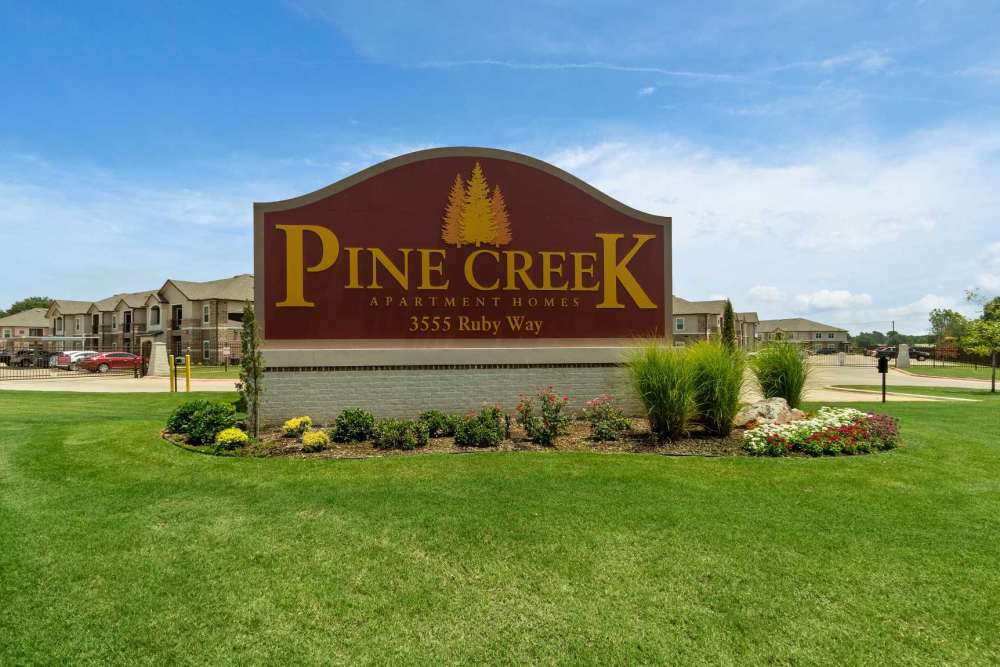 Exterior shot of apartments with property signage board at Pine Creek in Paris, Texas
