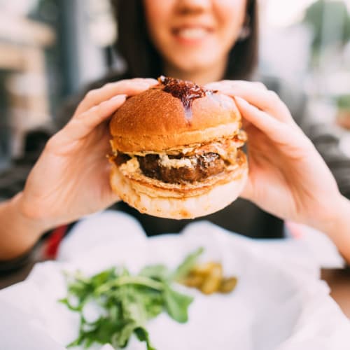 A woman holding up a burger at a restaurant near Huntsville Village Apartments in Huntsville, Texas