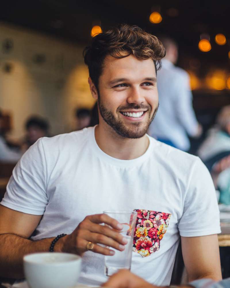A man with a warm smile sits at a table, savoring a glass of water at Caprock Crossing in College Station, Texas