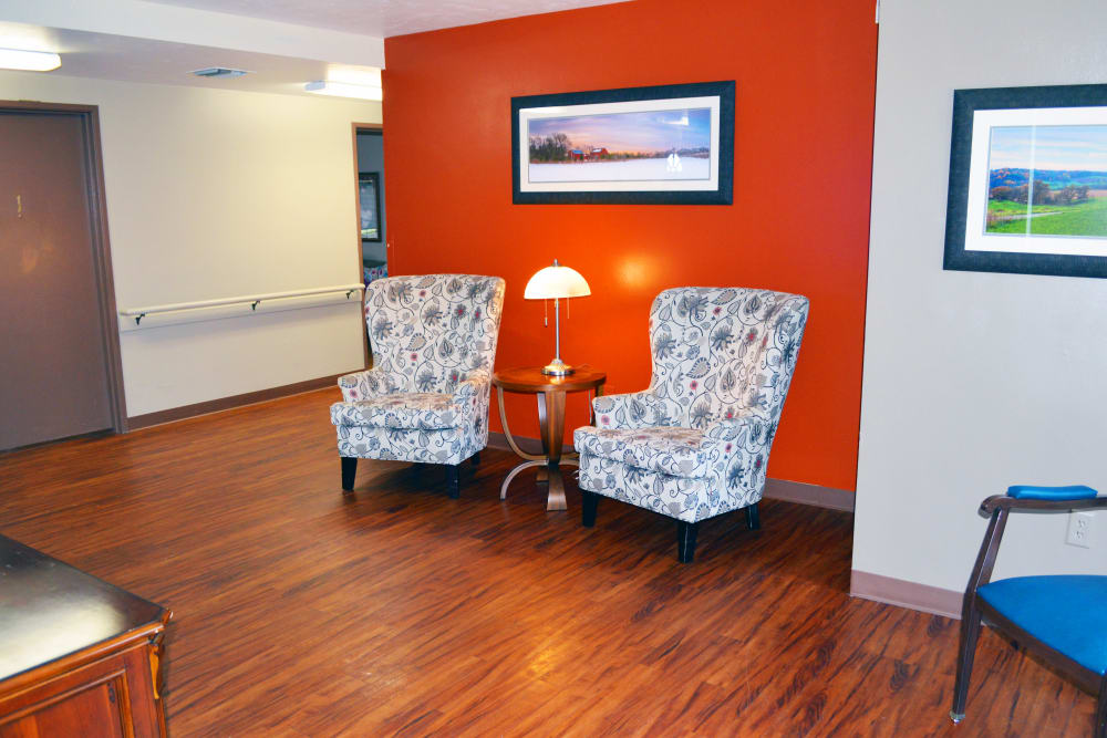 Lounge with cozy armchairs and bright red wall at Wyndemere Memory Care in Green Bay, Wisconsin. 