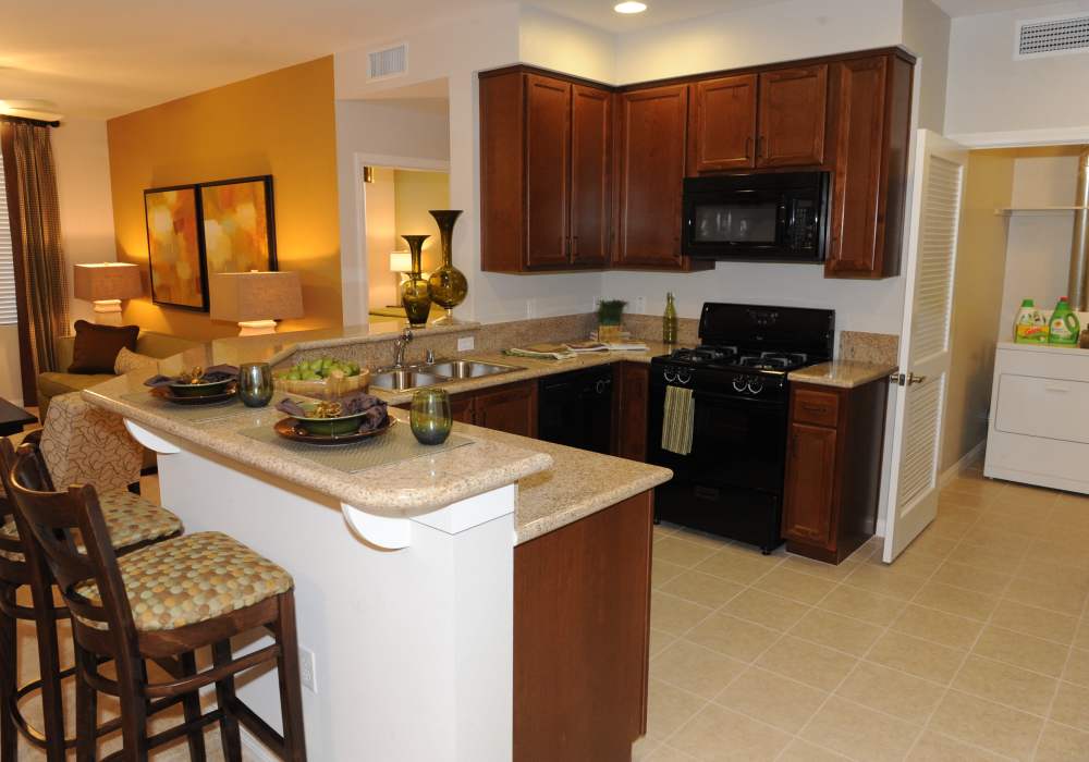 A modern kitchen featuring rich wood cabinetry, sleek black appliances, and a spacious breakfast bar, perfect for entertaining in a charming open-concept living space at Cresta Bella in San Diego, California