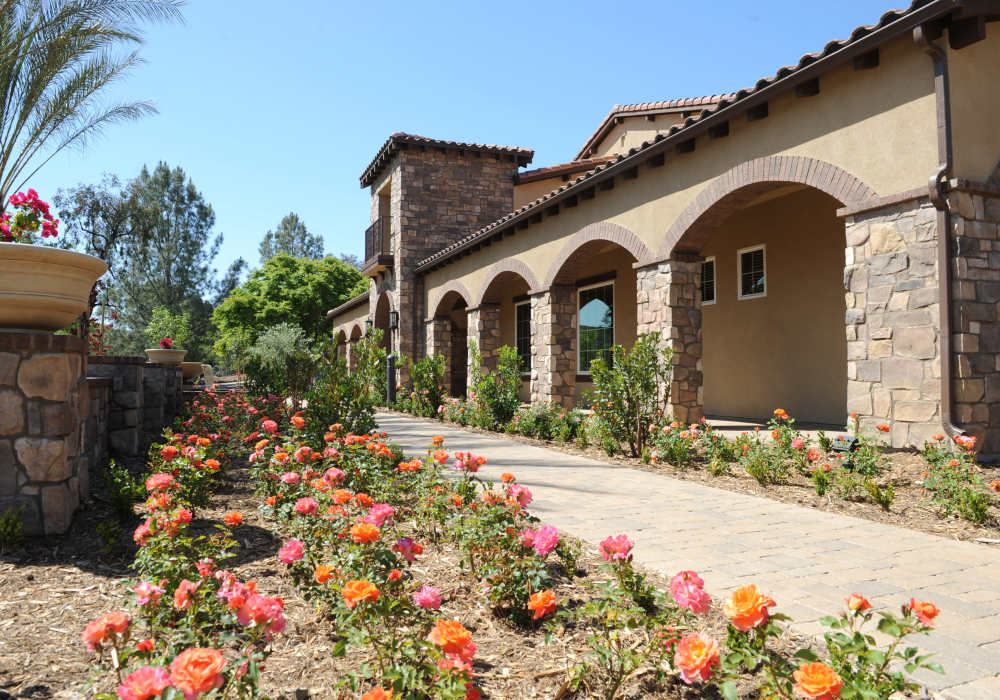 Charming stone-faced exterior framed by lush landscaping and vibrant rose gardens, inviting you into this exquisite home at Cresta Bella in San Diego, California