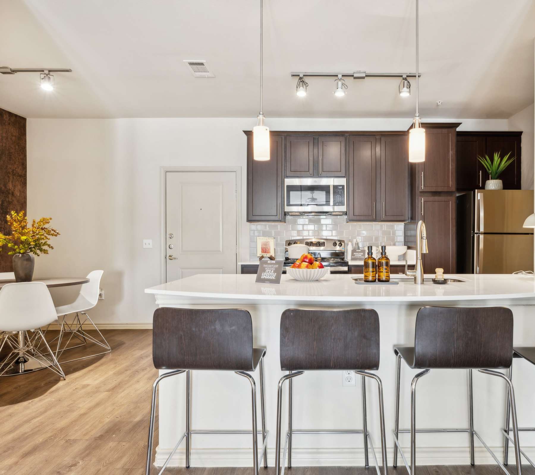 Modern kitchen with dark wood cabinets, stainless steel appliances, and a white island with bar stools at Midtown 905 in Denton, Texas