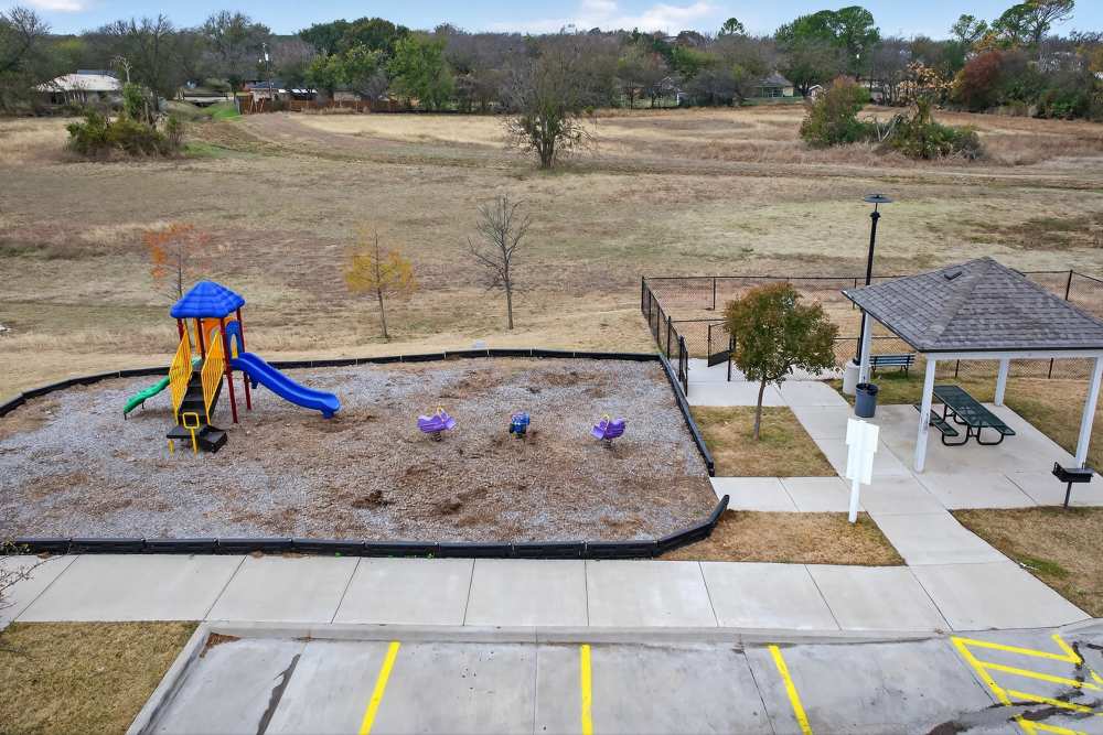 Charming playground with a colorful slide and swing set nestled beside a cozy gazebo, surrounded by lush green fields at Lakewood Crossing in Granbury, Texas.