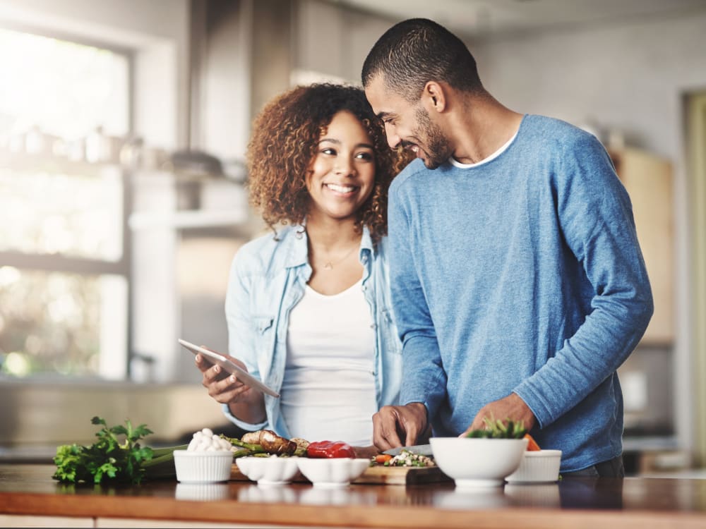 Resident couple looking up a recipe on a tablet while they cook a fresh meal in their new home at Sofi at Topanga Canyon in Chatsworth, California