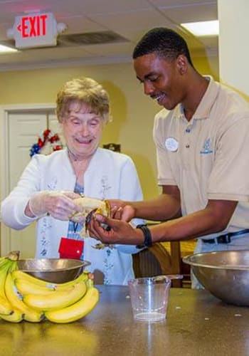 Resident getting help from a caretaker, preparing a treat in the kitchen at The Retreat at Lady's Island in Beaufort, SC