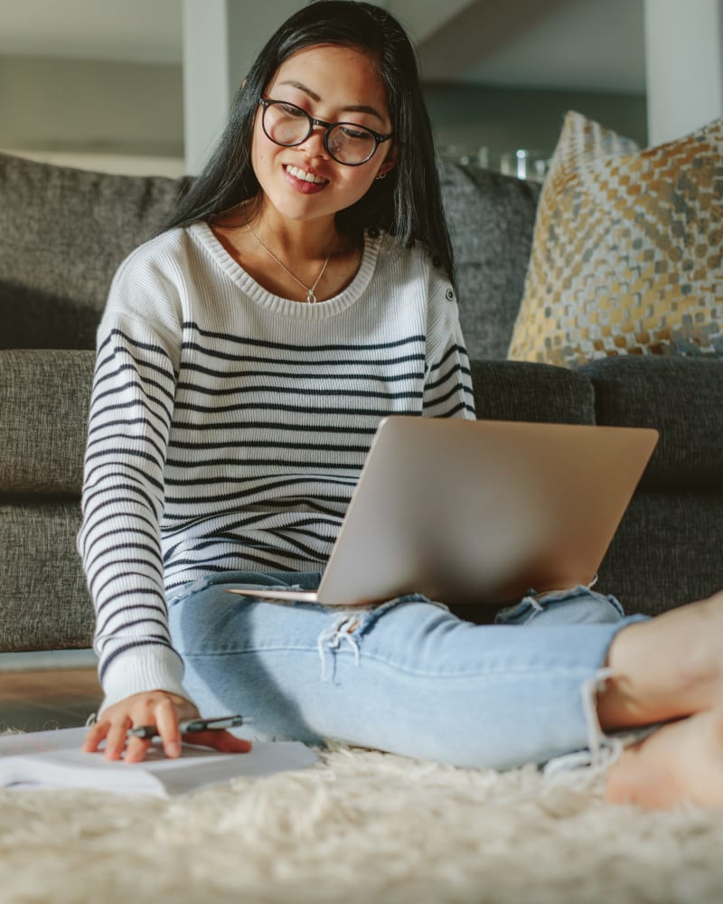 A woman sitting on her apartment floor with her laptop and a textbook at Mason Drive Apartments in Columbus, Georgia