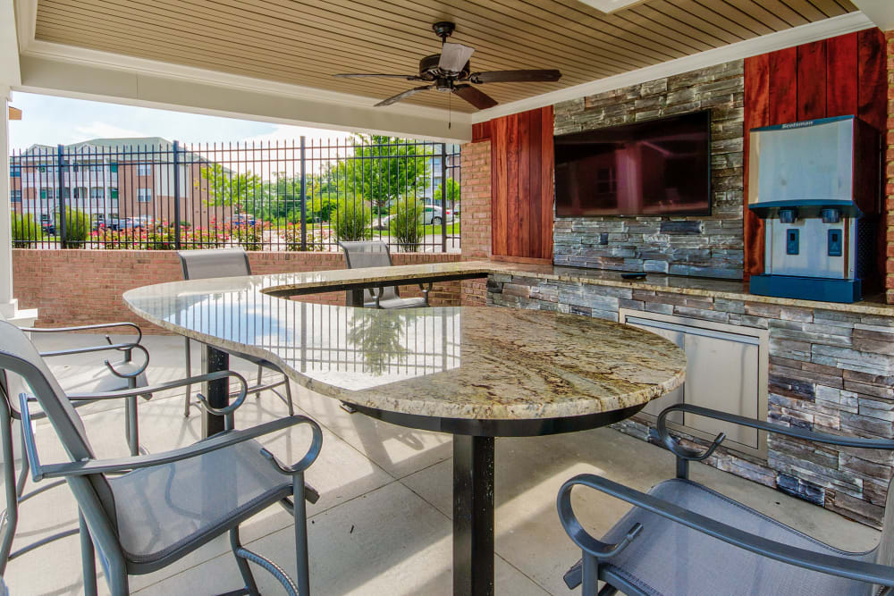 Table and chairs to sit in and watch tv in the covered area near the pool at Aspen Pines Apartment Homes in Wilder, Kentucky