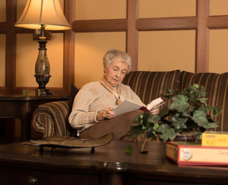 Resident sitting on a couch reading a book at York Gardens in Edina, Minnesota