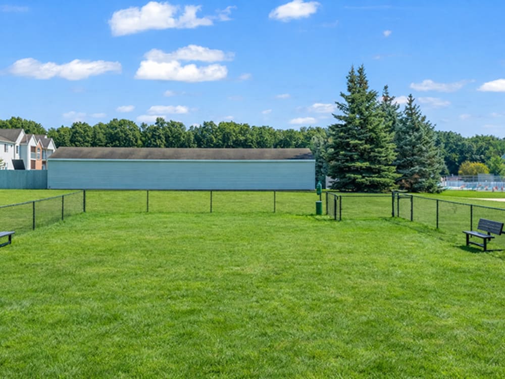 Fenced dog park with benches and green grass at Somerset Park Apartments in Bath, Michigan