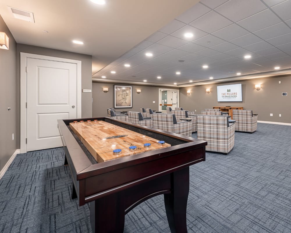 Resident entertainment room with television and shuffleboard at The Pillars of Hermantown in Hermantown, Minnesota